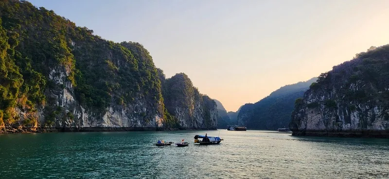 Small boats drift between towering limestone karsts at sunset in Lan Ha Bay near Cat Ba