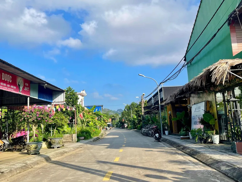 A quiet paved street lined with shops, potted plants, and thatched roofs under a blue sky in Cat Ba.