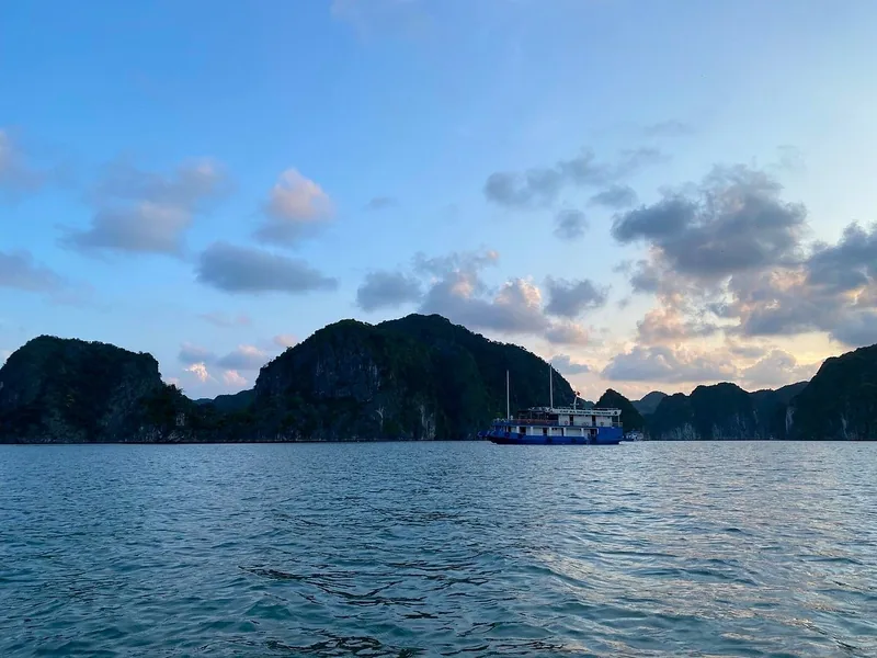 A cruise boat sails past limestone karsts under a soft evening sky in Lan Ha Bay near Cat Ba
