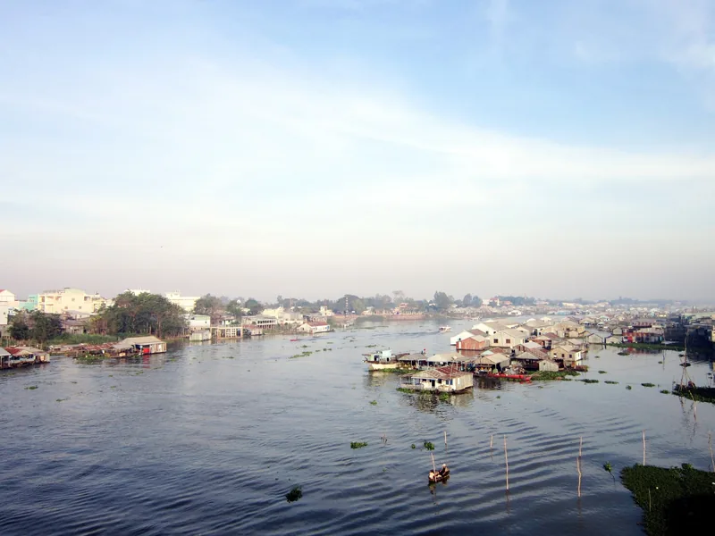 Floating houses and fish farms line the wide river at Chau Doc under a hazy sky.