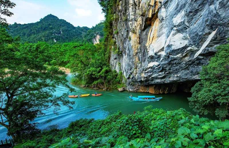Small boats glide along a jade-green river toward the karst cave entrance at Phong Nha in Vietnam.