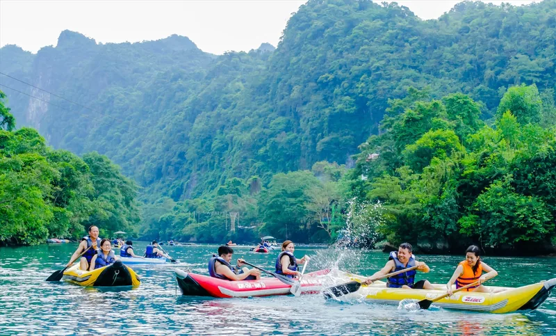 Tourists paddle colorful kayaks on a green river beneath limestone karsts near Phong Nha cave
