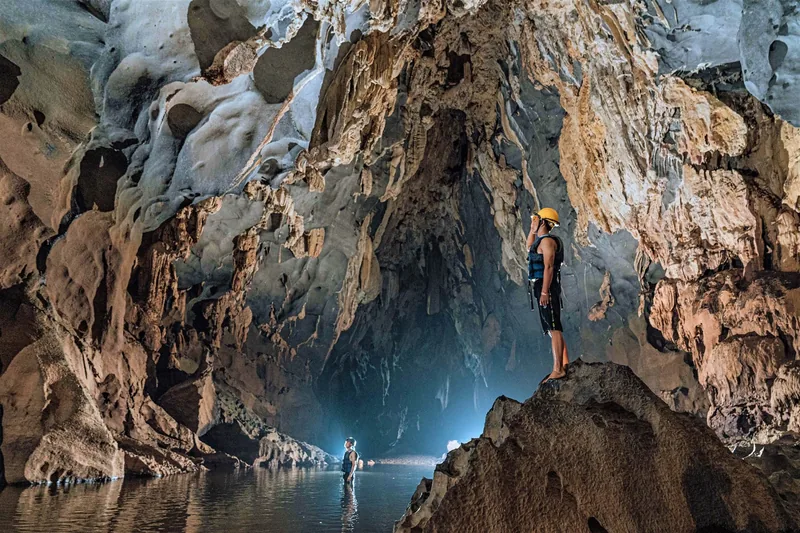 Adventurers wearing helmets and life vests explore a massive limestone cave with a river in Quang Binh.
