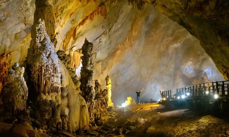 A visitor stands amid towering stalagmites inside Phong Nha Cave with a wooden walkway along the cavern floor.