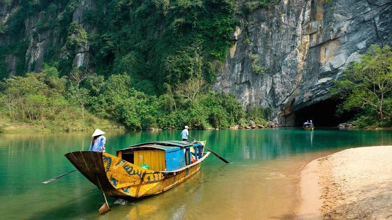 A traditional wooden boat glides on turquoise water toward the limestone cave entrance at Phong Nha.