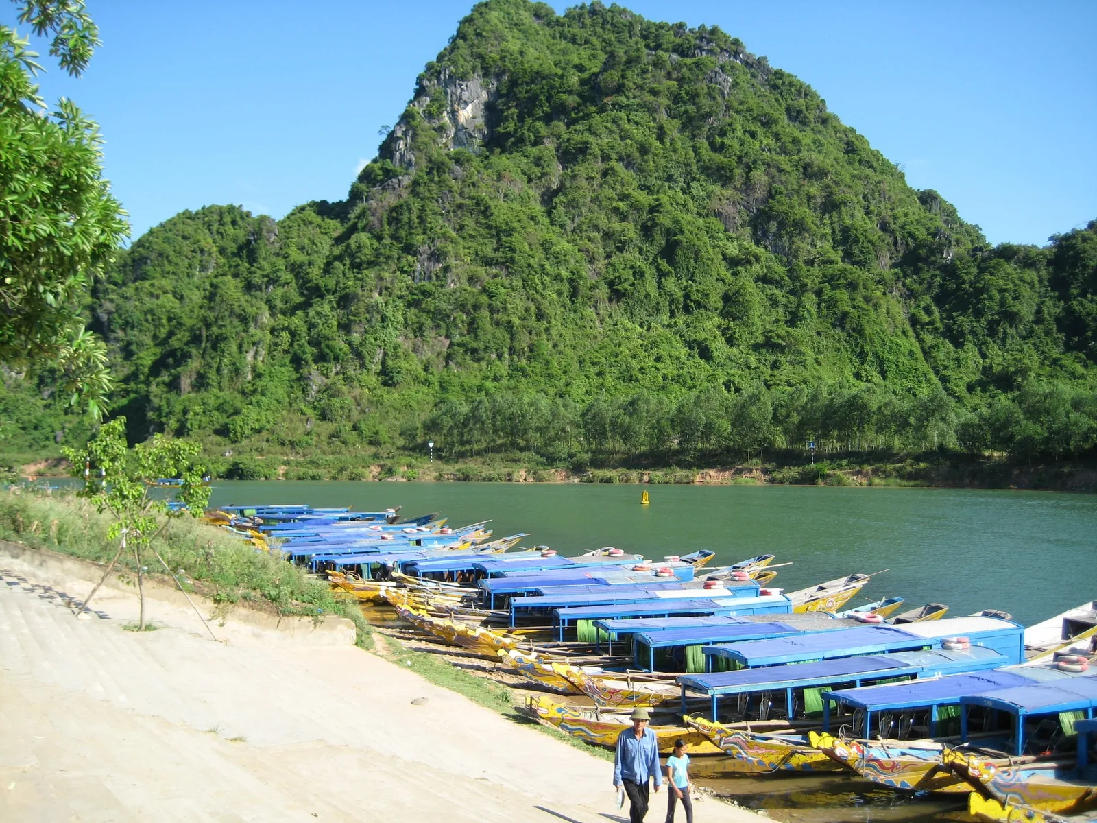 Blue-roofed tour boats line the riverbank beneath a limestone mountain in Phong Nha.