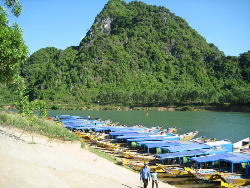 Blue-roofed tour boats line the riverbank beneath a limestone mountain in Phong Nha.